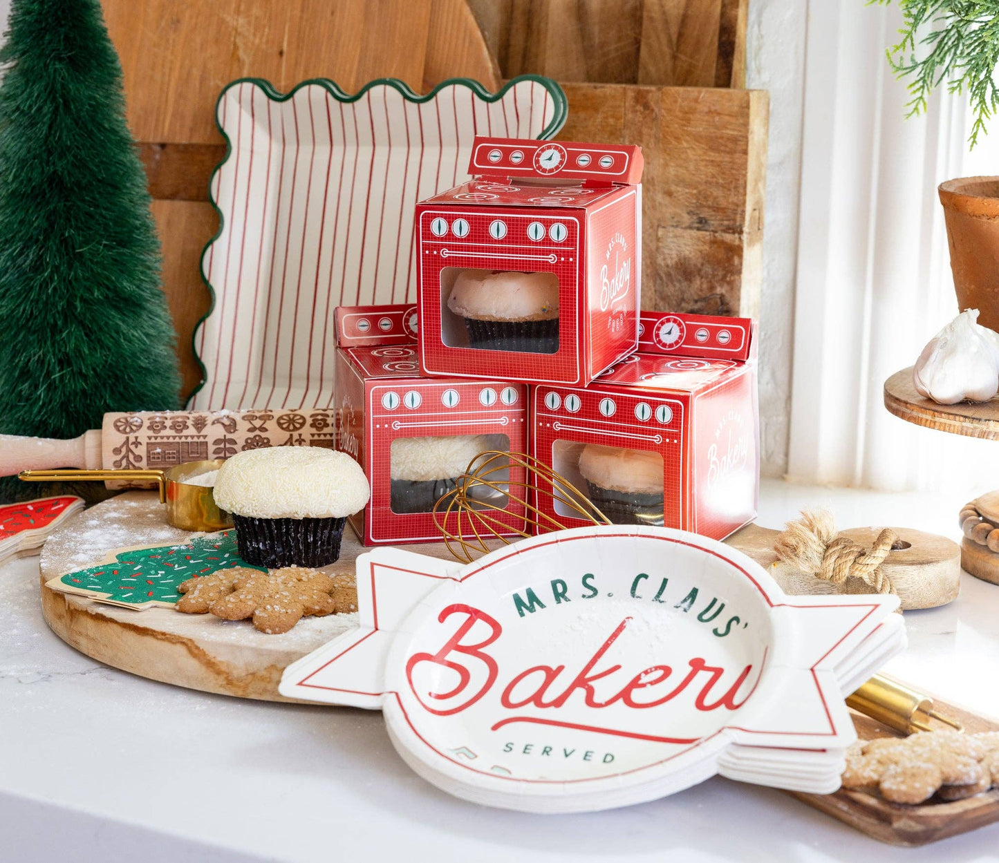 Red oven-shaped boxes with a 'Mrs. Claus Baker' sign on a festive table.