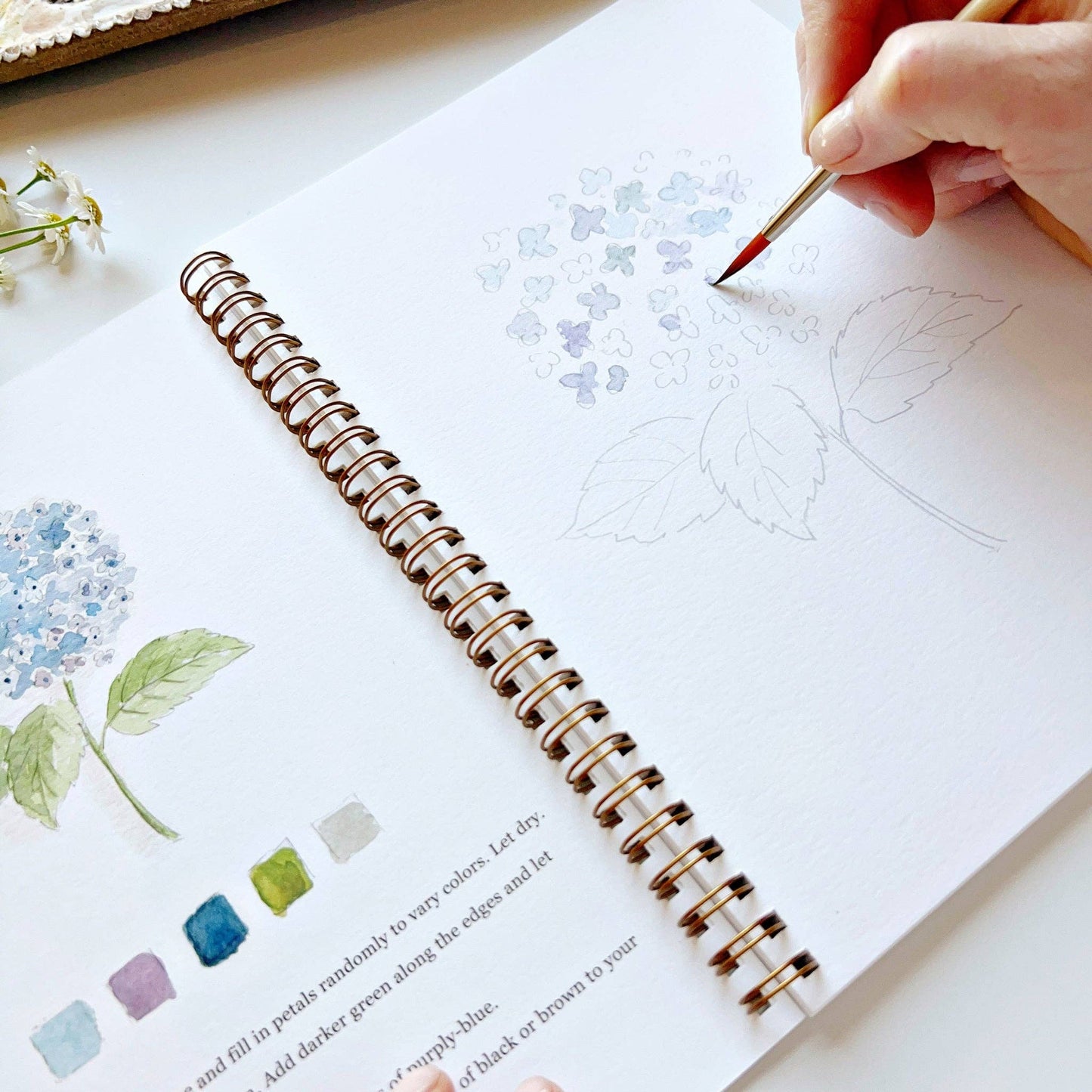 Person painting in a sketchbook with a paintbrush on a white surface