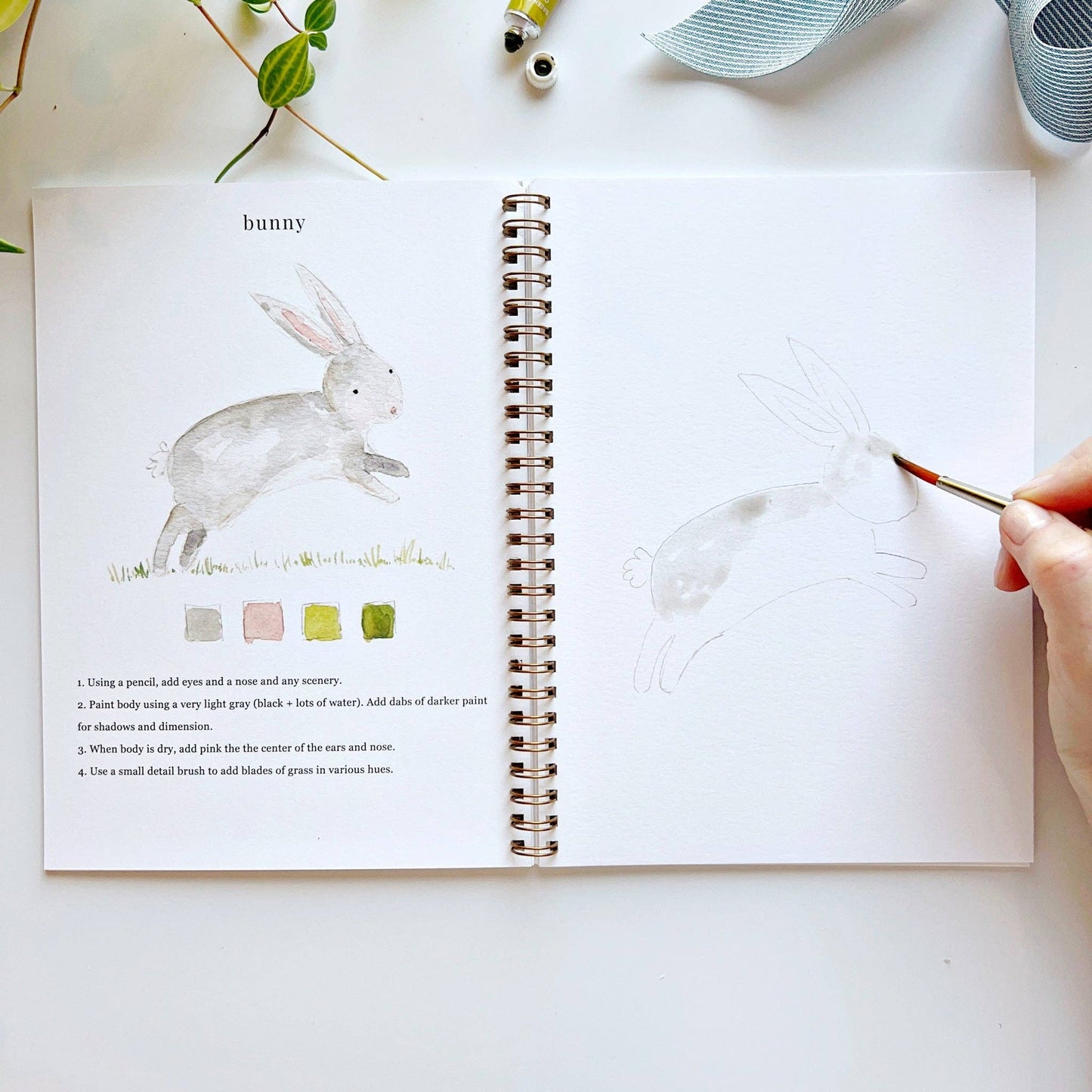 Open book with rabbit illustration and painting activity, hand holding paintbrush.