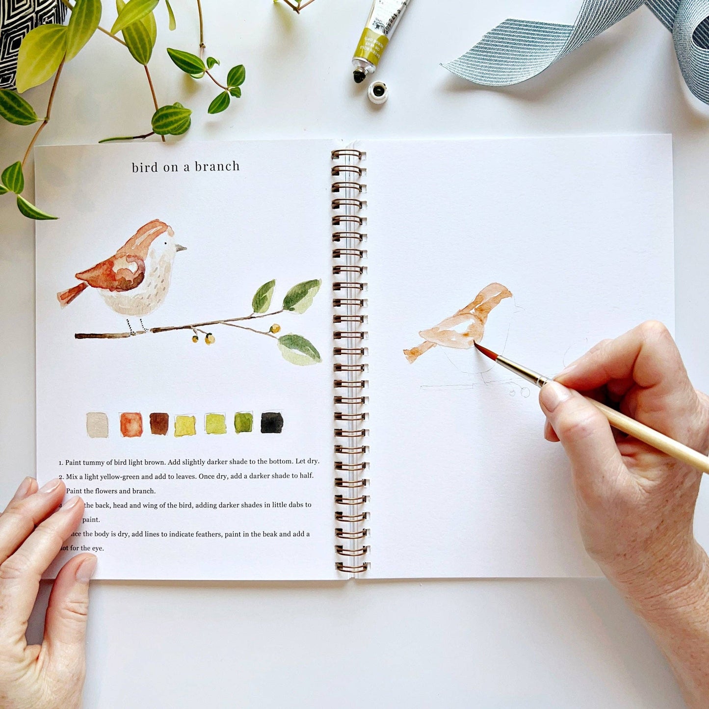 Person painting a bird illustration in a notebook with a paintbrush
