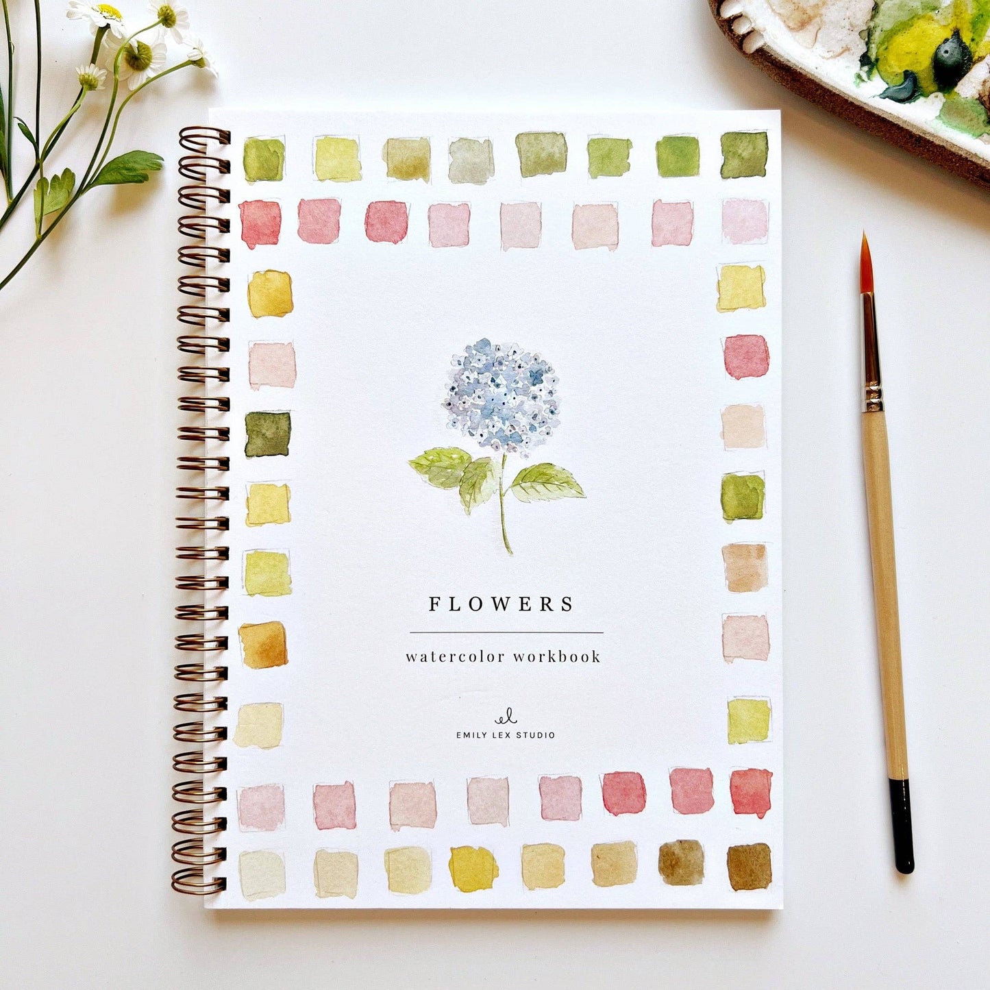 Watercolor workbook titled 'Flowers' by Emily Lex Studio on a white surface with a paintbrush and flowers.