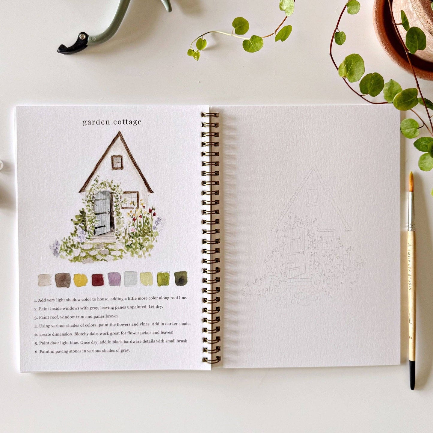 Open notebook with garden-themed illustration and color swatches on a white surface with greenery.