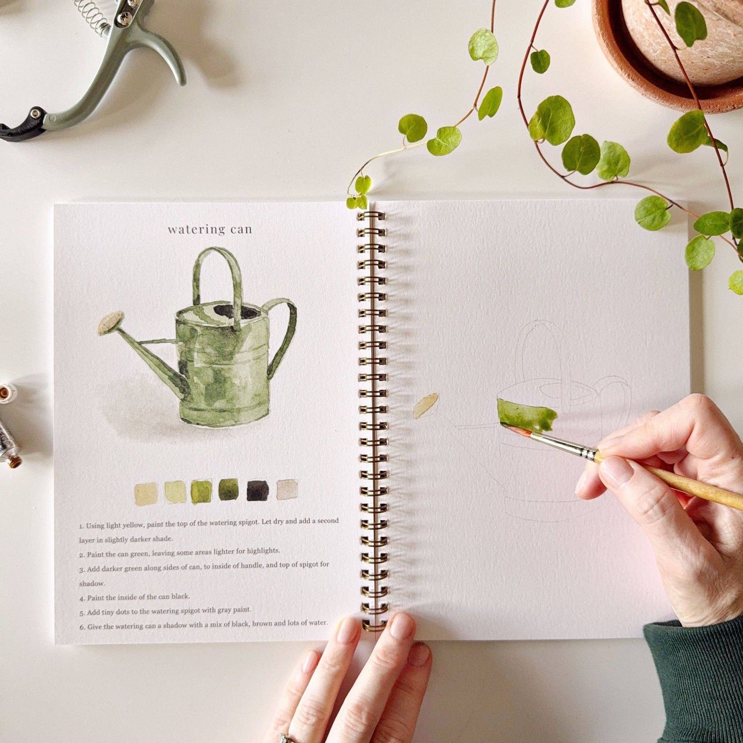 Open book with gardening illustration and hand holding a paintbrush