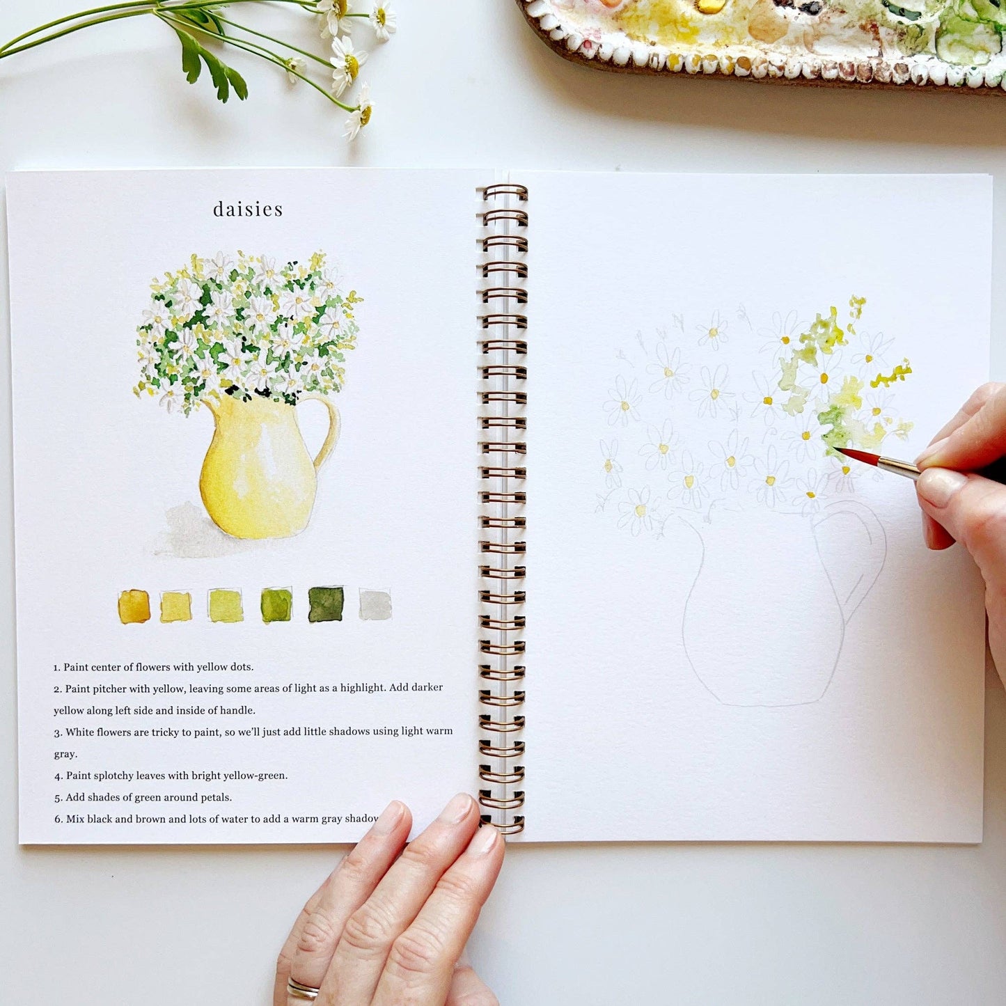 Open book with floral illustrations and color swatches, held by a person.