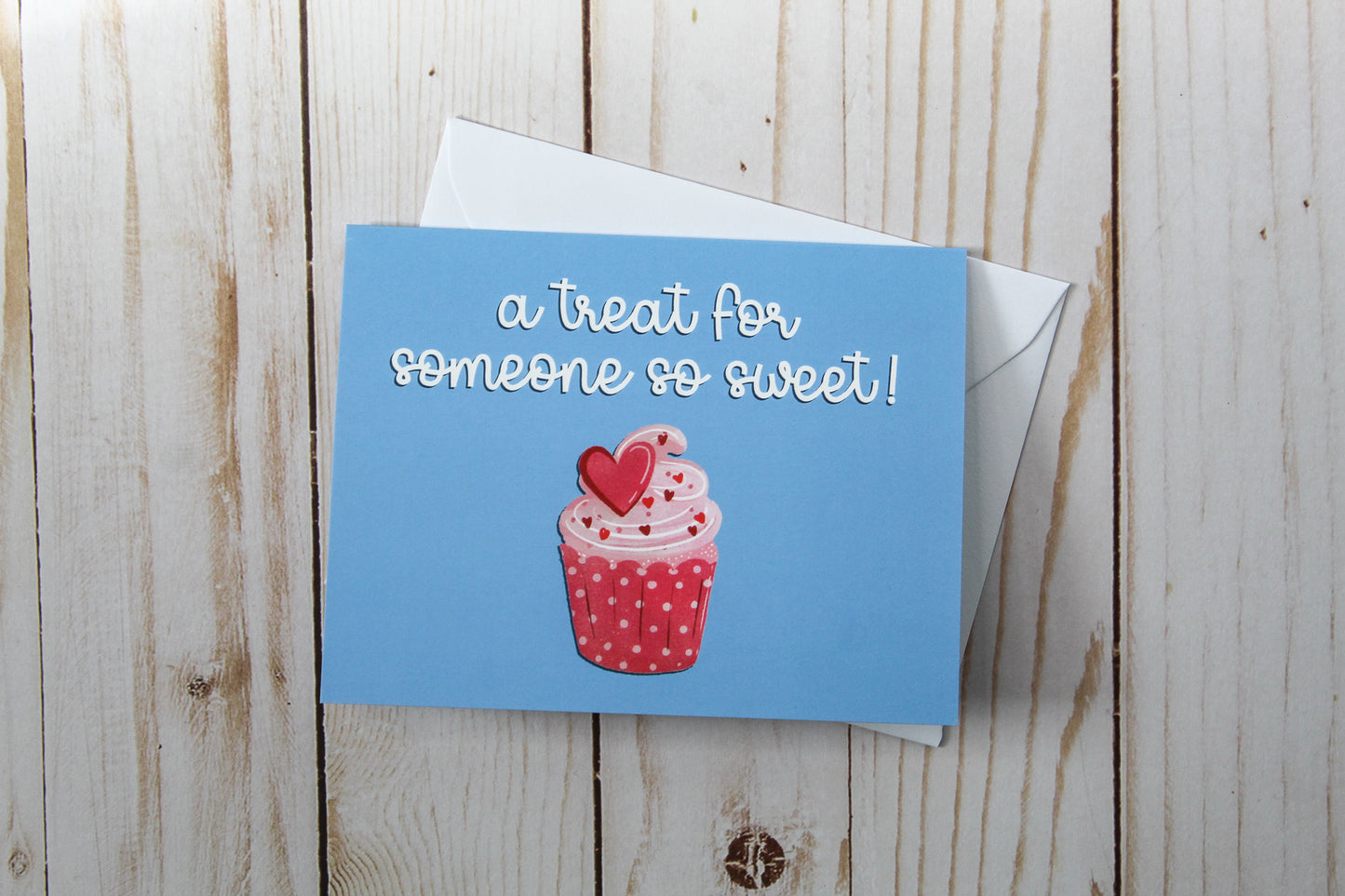 'A Treat For Someone So Sweet' card boasts a charming cupcake design against a blue backdrop. These cards are thoughtfully folded to a size of 4.25" in height by 5.5" in width, leaving the inside blank for your personal message.