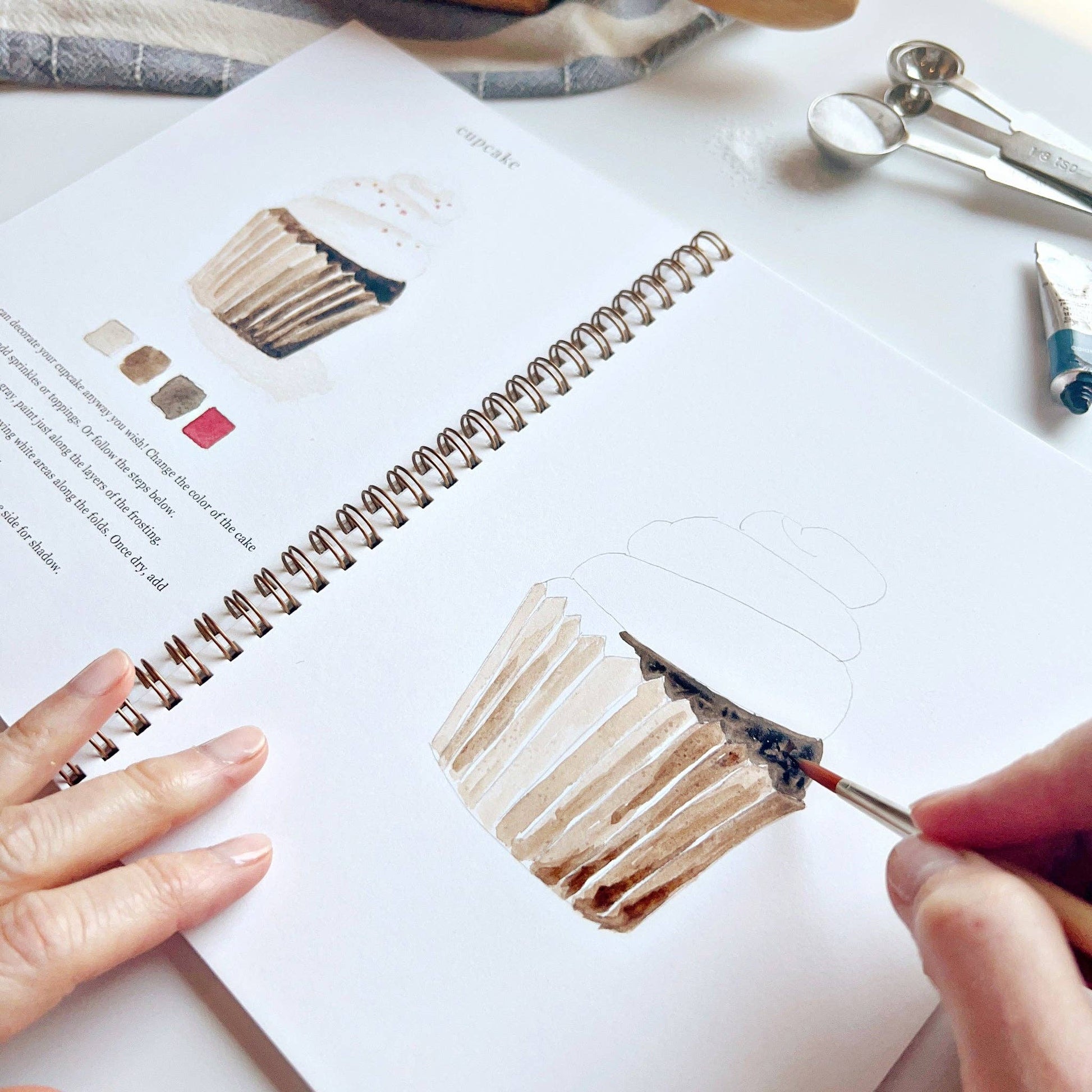 Person painting a brush stroke on a sketchbook with paint tools nearby