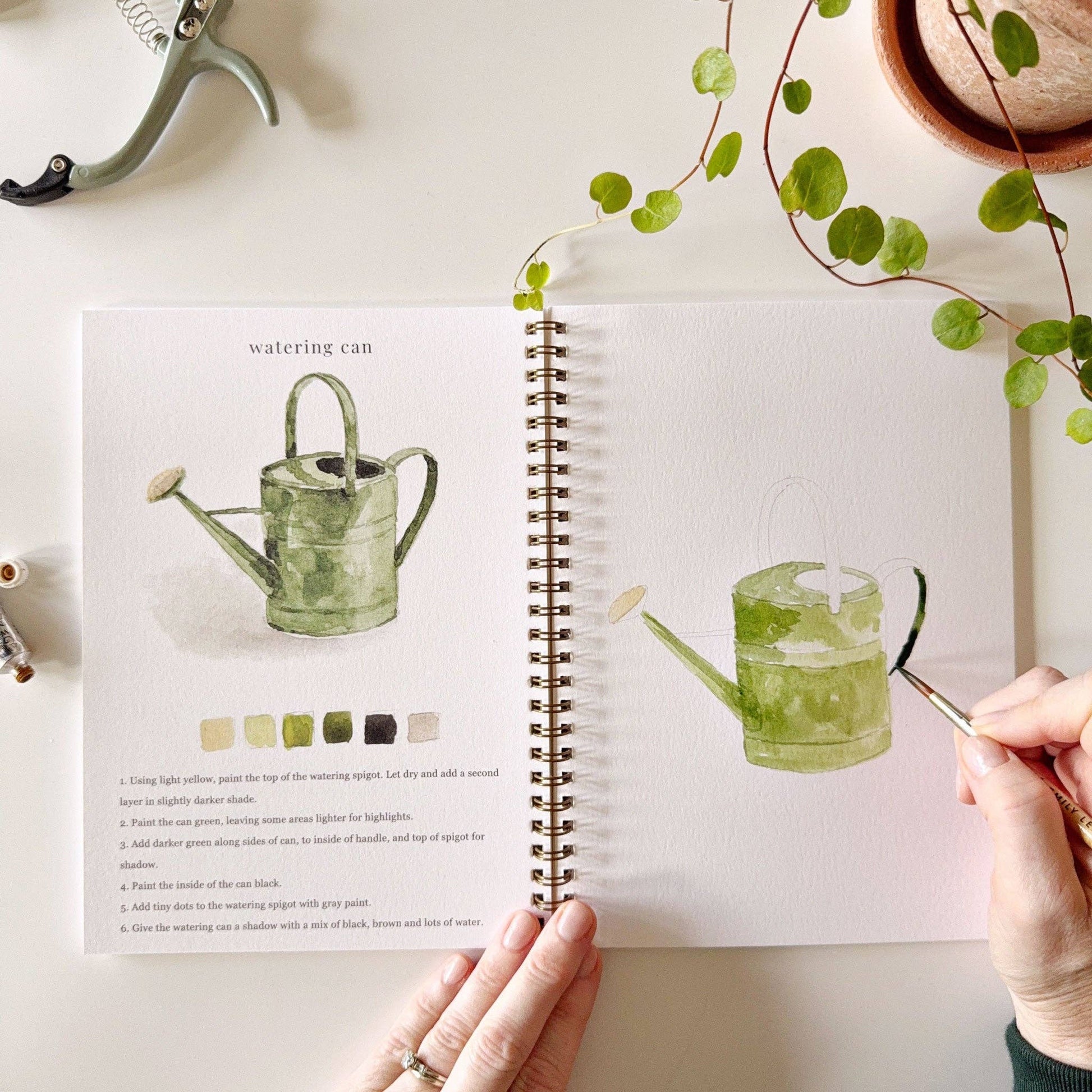 Open book with illustrations of a watering can held by a hand, with a plant in the background.