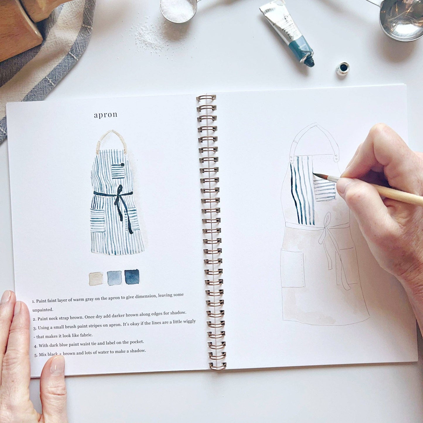 Person drawing an apron design in a notebook with a pencil.