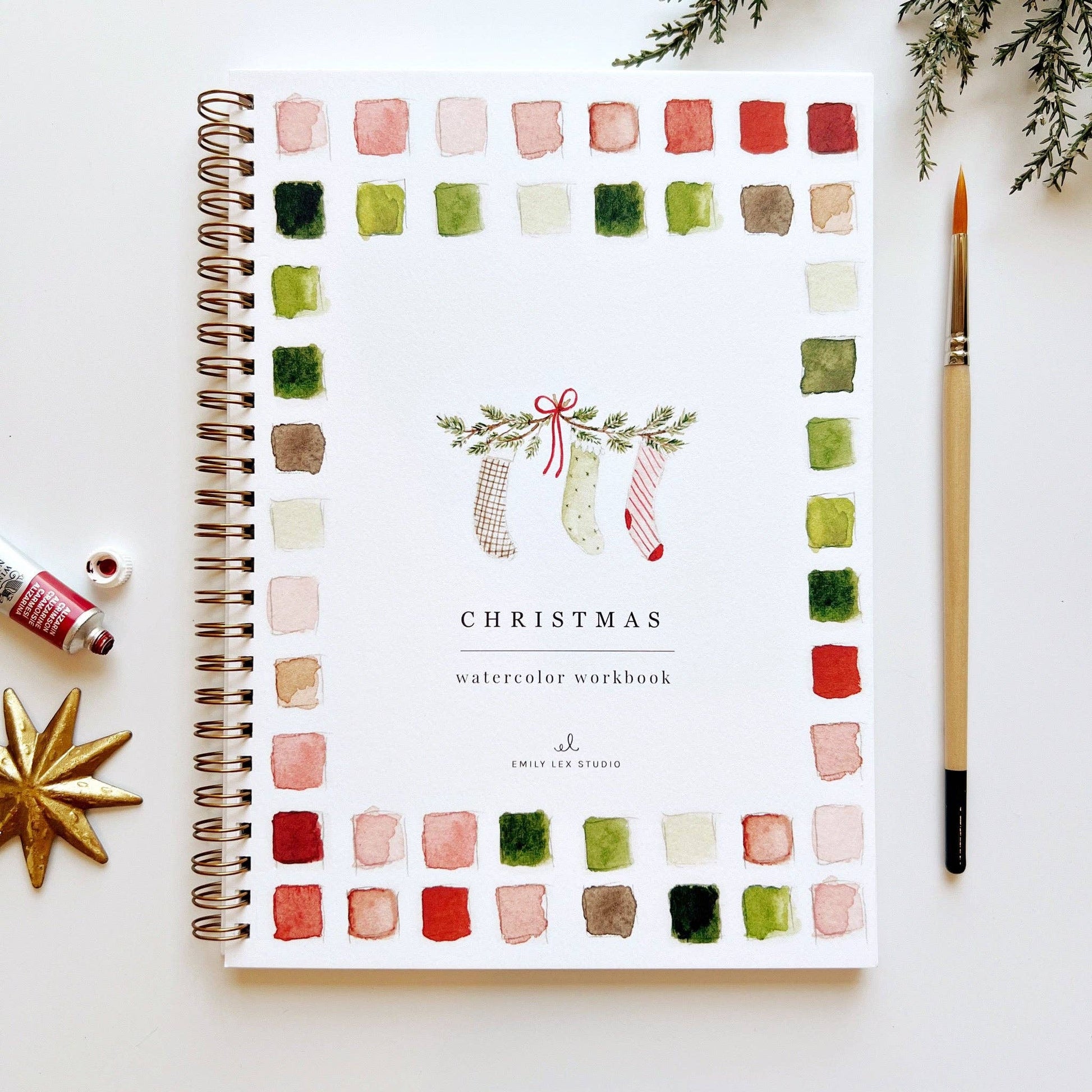 Christmas watercolor workbook with color swatches and a pen on a white surface.