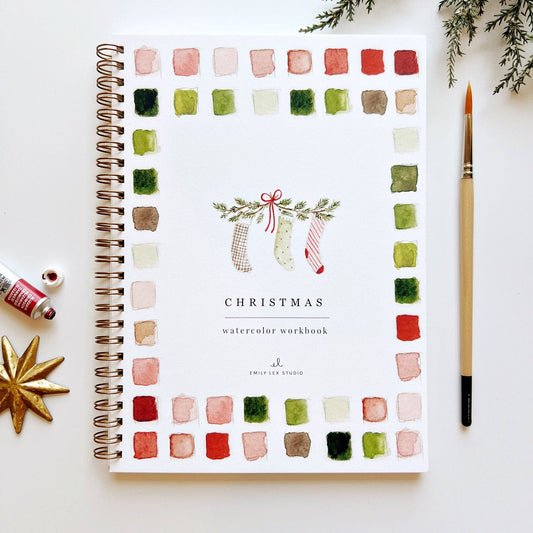 Christmas watercolor workbook with color swatches and a pen on a white surface.