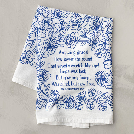 Flat lay of Amazing Grace tea towel with blue hymn lyrics on a farmhouse table