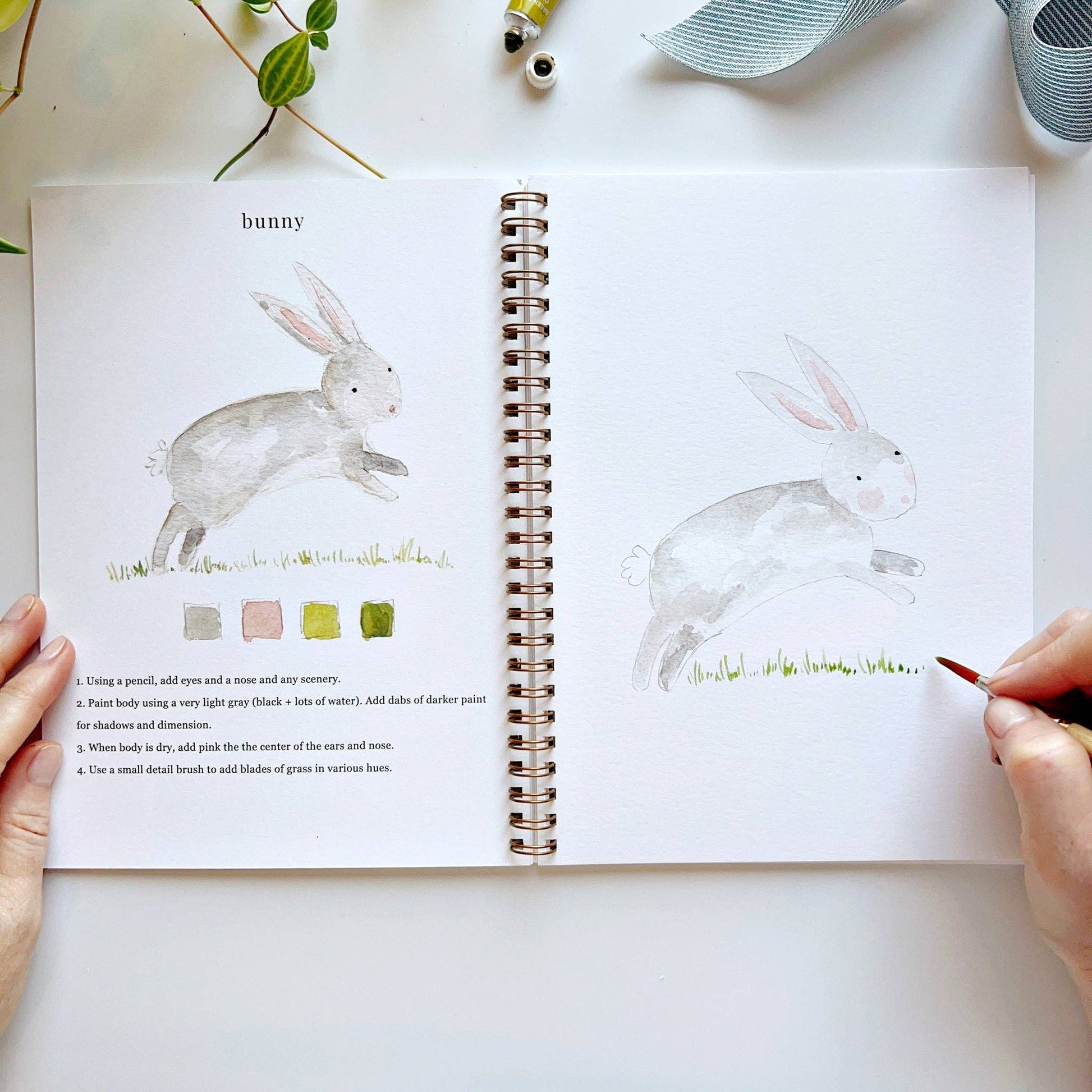 Open book with rabbit illustrations and painting guide on a white surface.