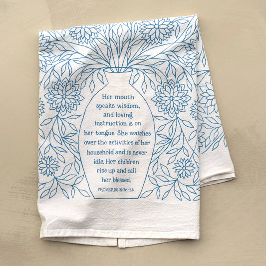 Flat lay of Proverbs 31 tea towel in light blue with scripture on wooden kitchen surface

