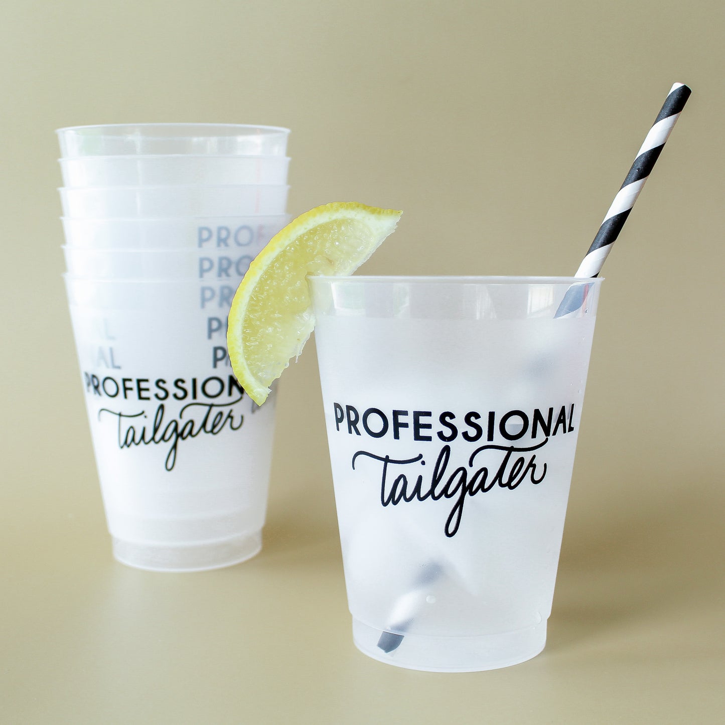 Two plastic cups with 'Professional Tailgater' text, a lemon wedge, and a straw on a beige background.