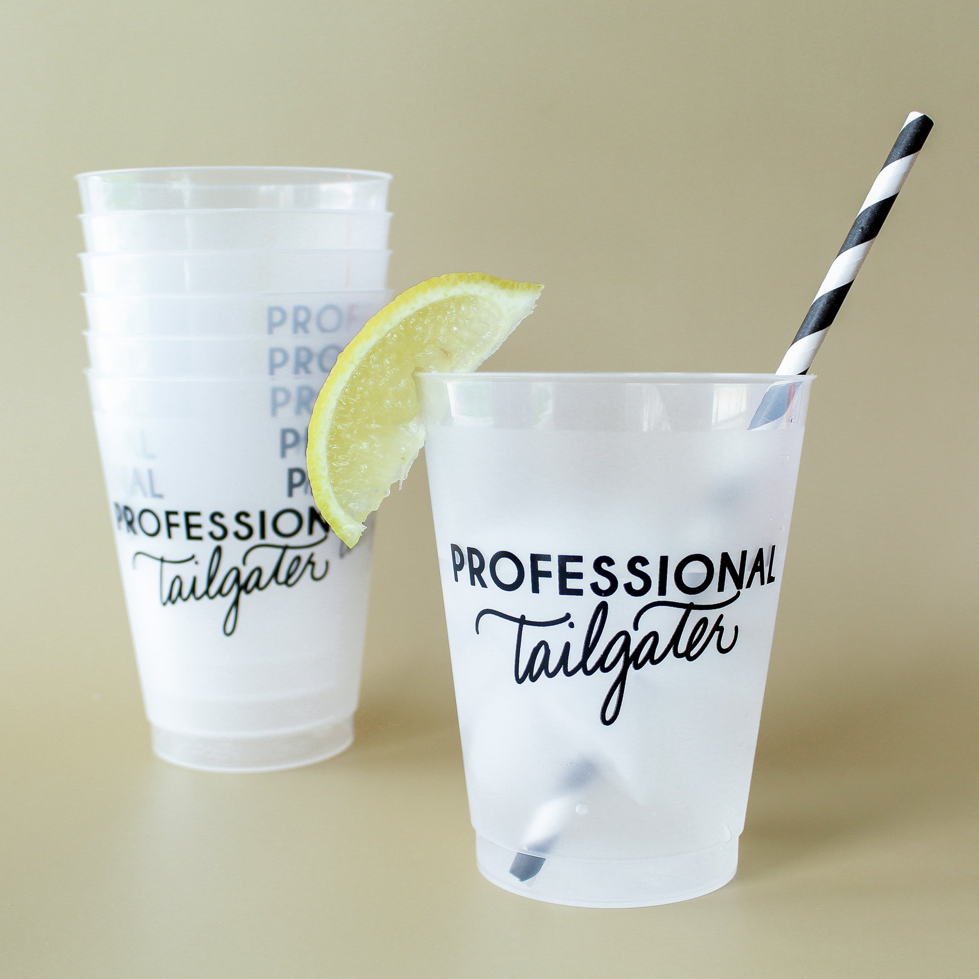 Two plastic cups with 'Professional Tailgater' text, a lemon wedge, and a straw on a beige background.