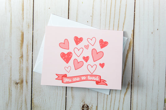 You Are So Loved' Valentine's Day Greeting card, adorned with charming hand-drawn hearts set against a lovely pink background