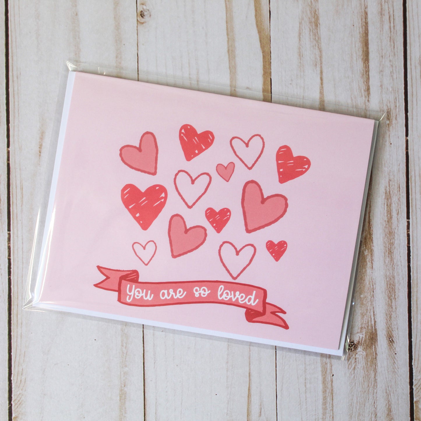 You Are So Loved' Valentine's Day Greeting card, adorned with charming hand-drawn hearts set against a lovely pink background