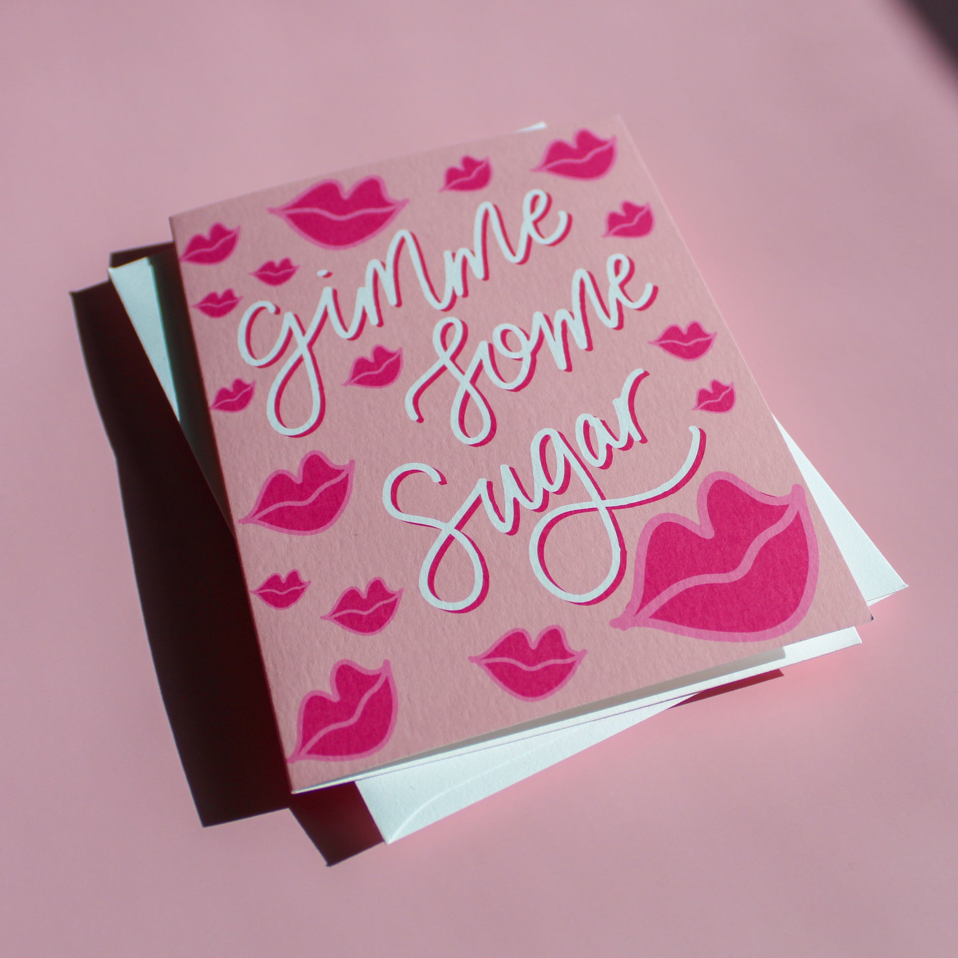 Our "Gimme Some Sugar" Valentine's Day card features hand drawn kissy lips on a pink background - it is perfect for a kid or adult! Each card is folded to 4.25" tall by 5.5" wide, is blank inside and comes with a matching white envelope. Cards are packaged in cellophane sleeves.